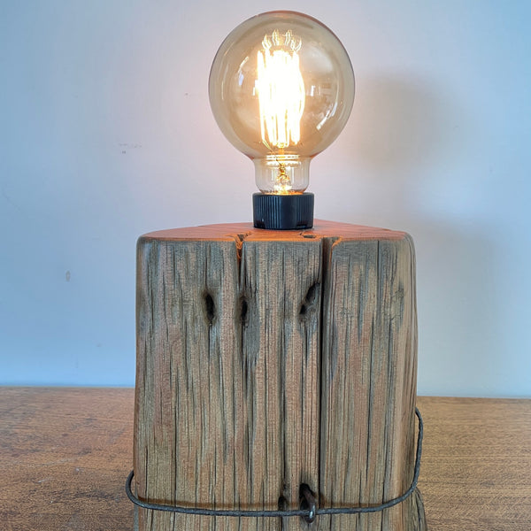 Heritage lamp upcycled from authentic totara post, with original No 8 wire, view of top half of front, with lit edison bulb.