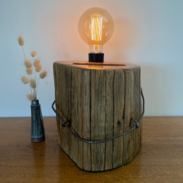 Heritage table lamp upcycled from large round hollowed out Tōtara post with No8 wire  and 2 original staples, front view, lit.