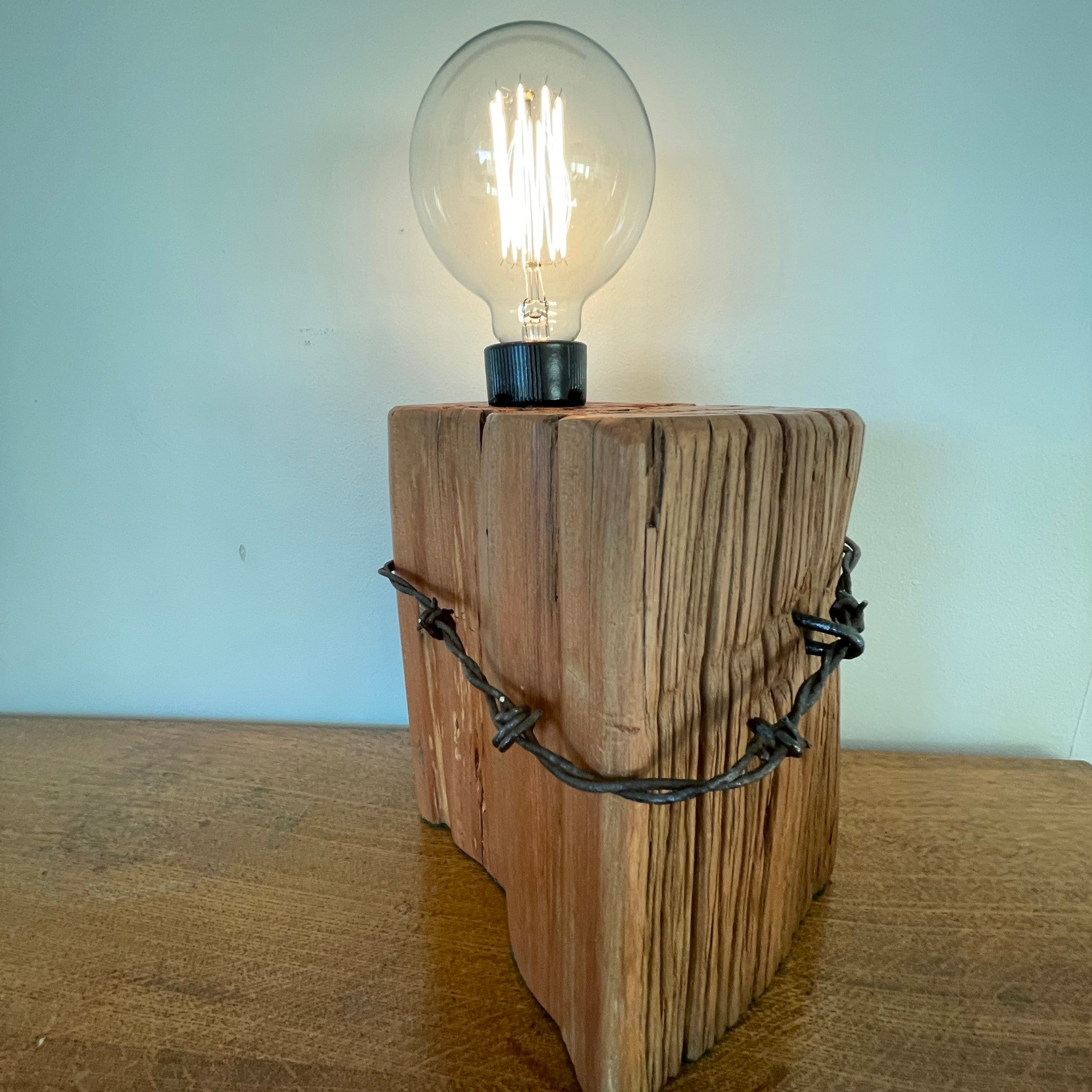 Hundred year old tōtara fence post, handcrafted by shades at grays with original barbed wire and additional edison bulb, lit.