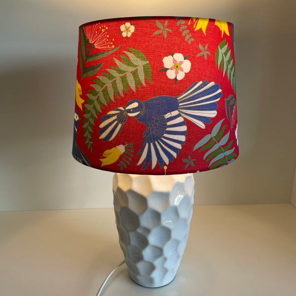 Jade Ell design on medium tapered lampshade with fantail dance on crimson red fabric, handcrafted by shades at grays, lit, on white base.