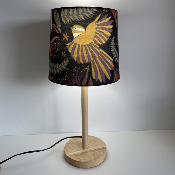 Jade Ell designed fantail dance on midnight black fabric on small tapered lampshade, handcrafted by shades at grays, lit on wooden stand.