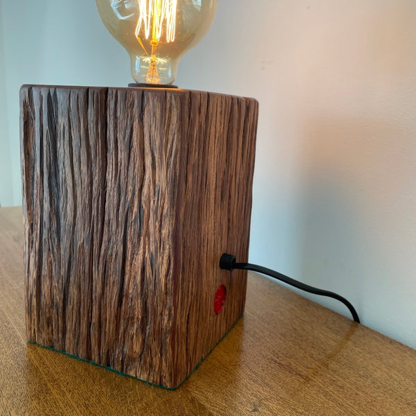 Jarrah wood table lamp handcrafted by shades at grays, teamed with a replica edison bulb, lit, back and side view.