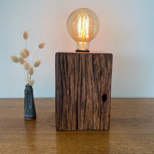 Jarrah wood table lamp handcrafted by shades at grays, teamed with a replica edison bulb, lit, front view.