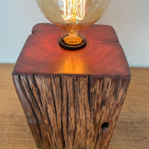 Jarrah wood table lamp handcrafted by shades at grays, teamed with a replica edison bulb, lit, top and front view.