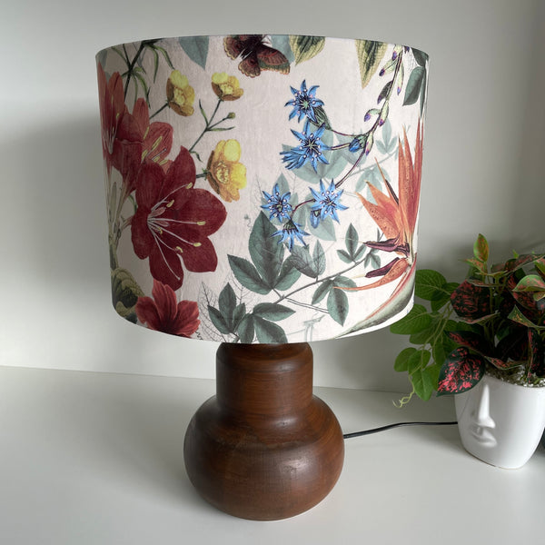 Large drum lampshade handcrafted by shades at grays with velvet fabric showing dainty blue and yellow flowers and bold red and orange blooms on a cream background, unlit.