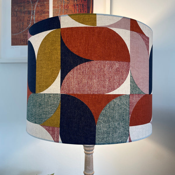 Large drum lampshade in bold and beautiful fabric based on geometric pattern, and variety of colours, lit, handcrafted by shades at grays.