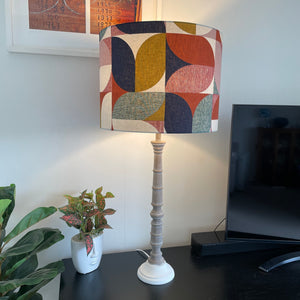 Large drum lampshade in bold and beautiful fabric based on geometric pattern, lit, on tall grey wooden lamp base, shade is handcrafted by shades at grays.