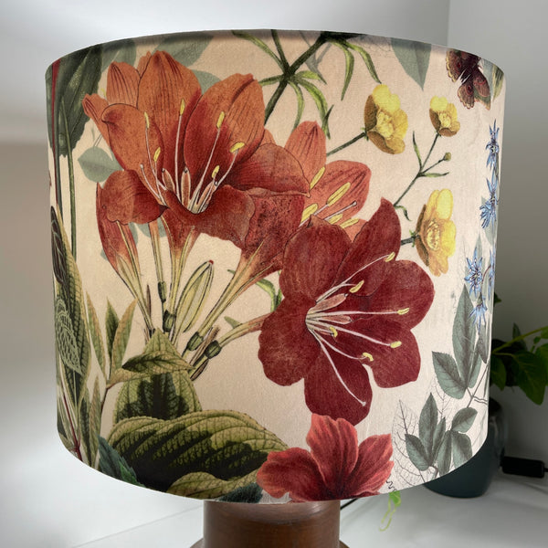 Large drum lampshade, lit, handcrafted by shades at grays with velvet fabric and close up of bold red flowers among foliage on a cream background.
