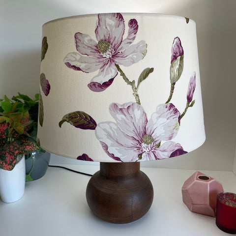 Large tapered handcrafted lampshade by shades at grays with magnolia purple fabric on short brown base, lit.