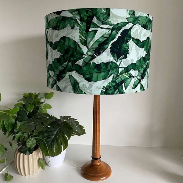 Large barrel bespoke lamp shade with a banana leaves fabric on wooden stand, unlit.