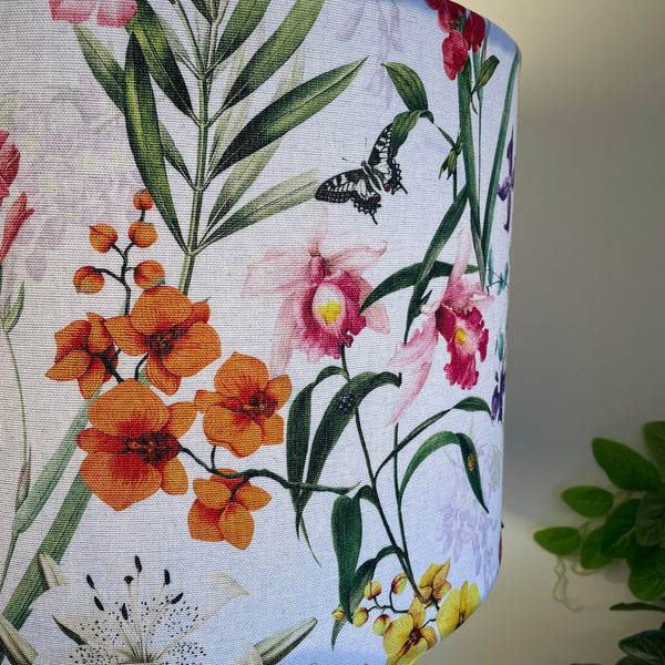 Large drum handcrafted fabric lamp shade made in nz by shades at grays using spring orchids fabric, close up of ornage orchid and butterfly, lit.