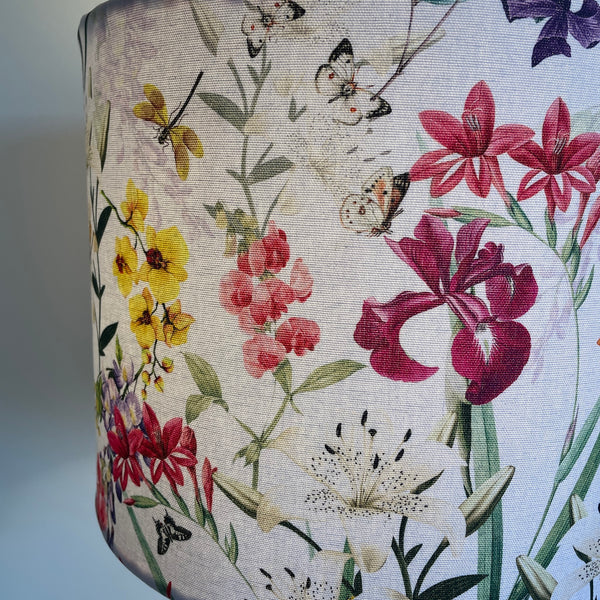 Large drum handcrafted fabric lamp shade made in nz by shades at grays using spring orchids fabric, close up of white butterflies among pink flowers, lit.