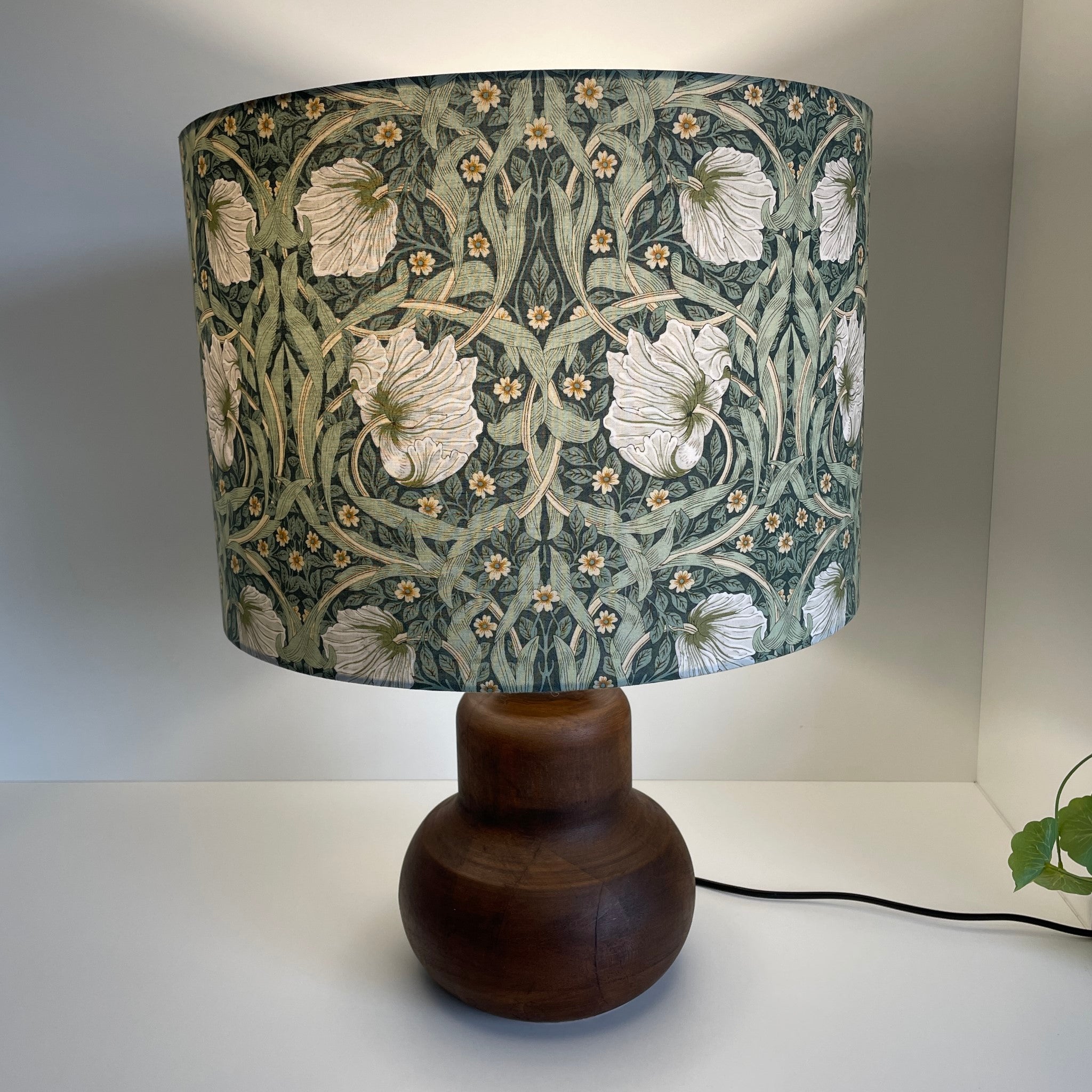 Large drum in Morris pimpernel olive fabric on brown base, lit by shades at grays.