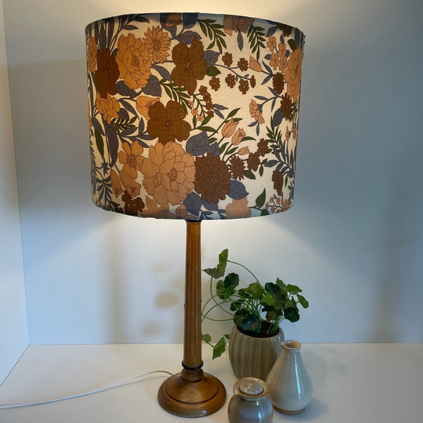 Large drum lamp shade made in nz by shades at grays, mid century brown floral print, lit. on wooden table lamp base.