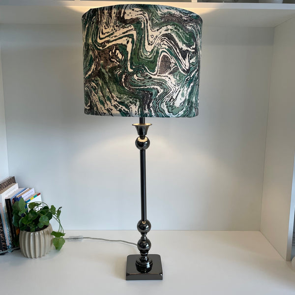 Large drum style lampshade with greywacke fabric, lit, on tall brushed metal base.
