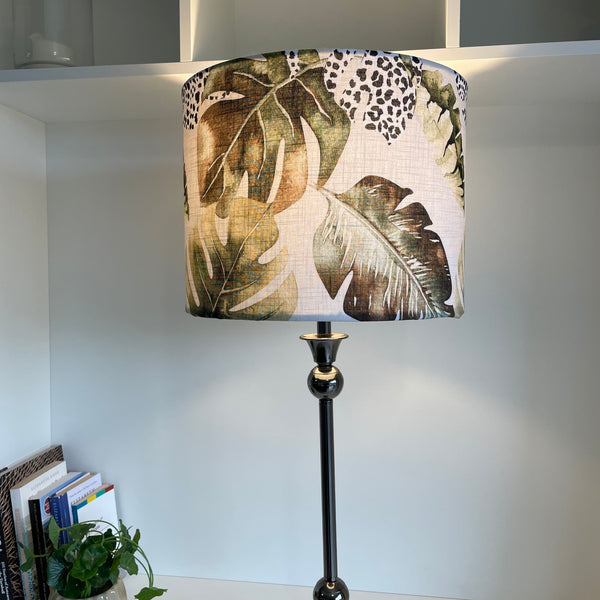 Large drum style light shade with jungle chic fabric on silver lamp base, lit.