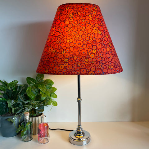 Large lamp shade handcrafted by shades at grays in nz with Kaffe Fassett button mosaic ornage fabric, lit on silver base.