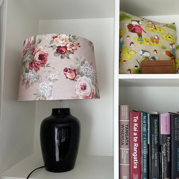 Large tapered ready made lampshade in vintage flower fabric, on black ceramic base on shelf unit.