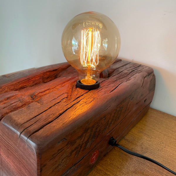 Large wood table lamp crafted by shades at grays from wharf timber with original nail and replica edison bulb, back and side view.