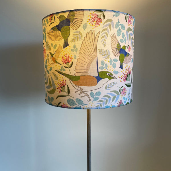 Medium cylinder lampshade with Jade Ell's Tauhou Silvereye Birds fabric, handcrafted by shades at grays, lit.