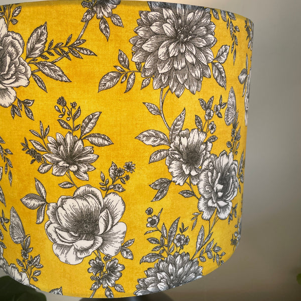 Medium drum handcrafted by shades at grays with floral glow fabric, lit close up of white and black flowers on a daffodil yellow background.