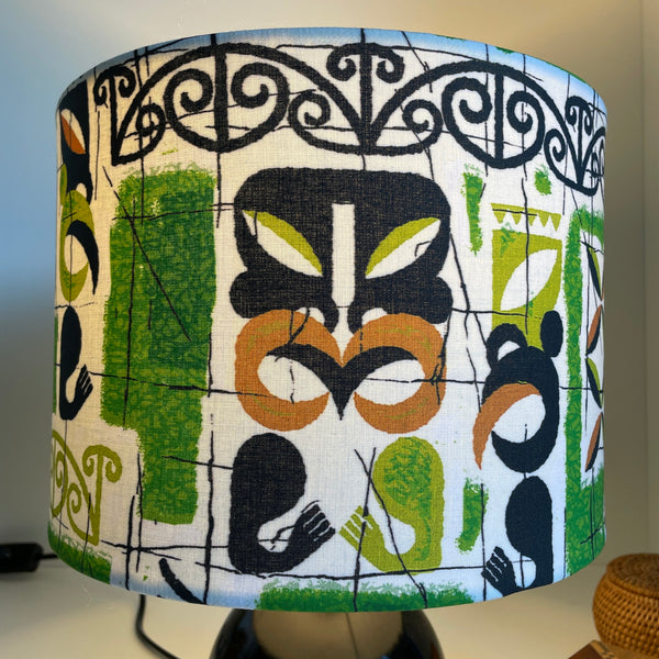 Medium drum lampshade in tiki vivid fabric by shades at grays, lit, close up.