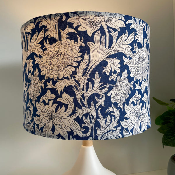 Medium drum lampshade with Morris Chrysanthemum Tonal Blue fabric on white lamp base, lit, on white base by shades at grays nz.
