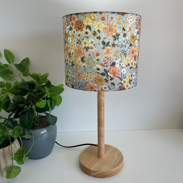 Medium drumshade floral mix fabric, lit, on a medium wood stand, sold by shades at grays. 