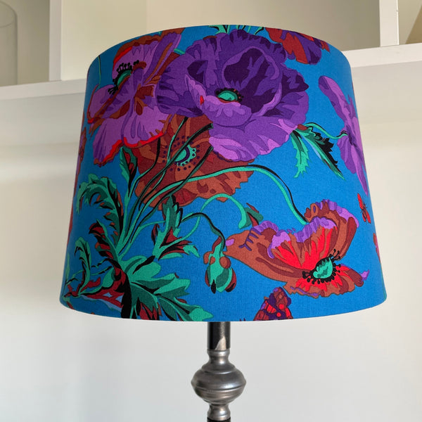 Medium tapered lampshade handcrafted by shades at grays with Kaffe Fassett teal meadow fabric, with intense red and purple flowers, unlit.