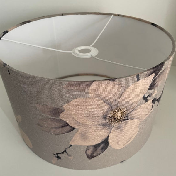 Medium barrel lampshade with large magnolia flowers on a grey background, ceiling pendant, unlit.