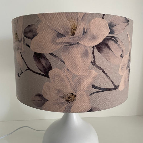 Medium barrel lampshade with large magnolia flowers on a grey background, on a white table lamp,unlit.