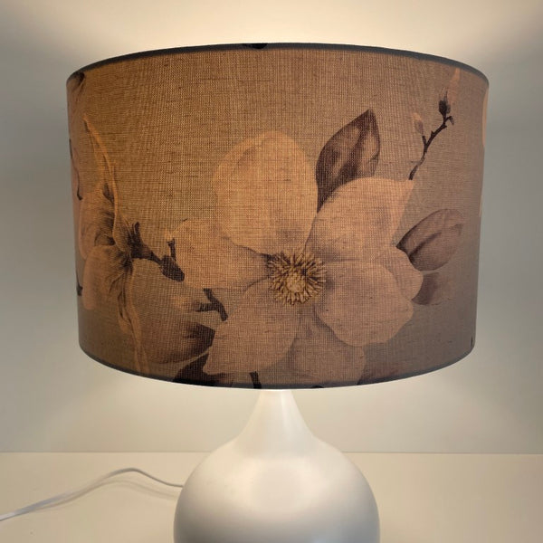 Medium barrel lampshade with large magnolia flowers on a grey background, table lamp,lit.