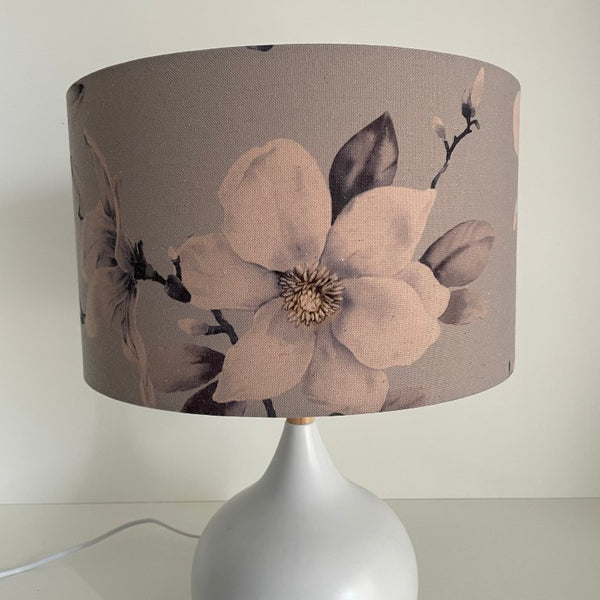 Medium barrel lampshade with large magnolia flowers on a grey background, table lamp,unlit.