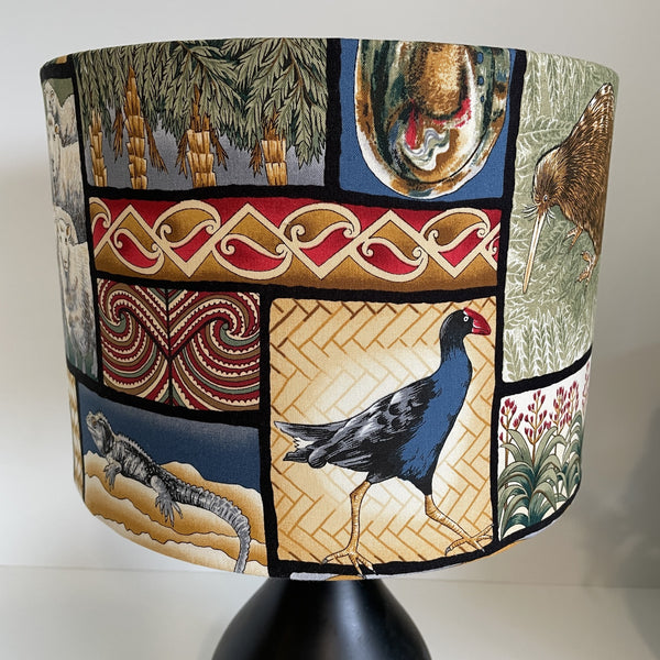 Decorative lampshade with New Zealand māori designs, birds and flora, lit.
