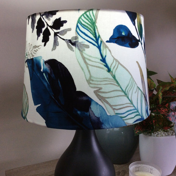 Medium tapered handcrafted fabric lamp shade with watermark palm fabric, lit.