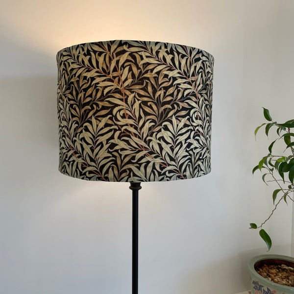 Medium size drum style lampshade with William Morris Willow Boughs black fabric, lit, on black lamp base by shades at grays, nz.
