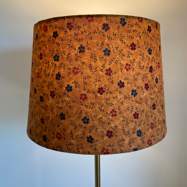 Medium tapered lampshade with cornflowers on brown background, handcrafted by shades at grays, lit.