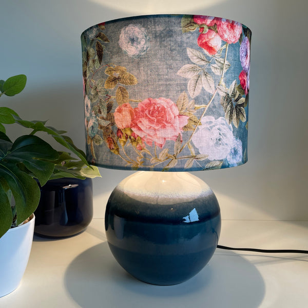 Ocean blue floral bespoke lamp shade on ceramic round lamp base, lit.