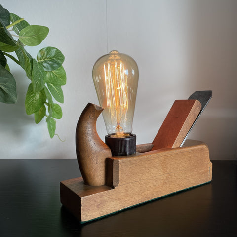 Original vintage wood plane lamp with edision bulb, lit, by shades at grays.