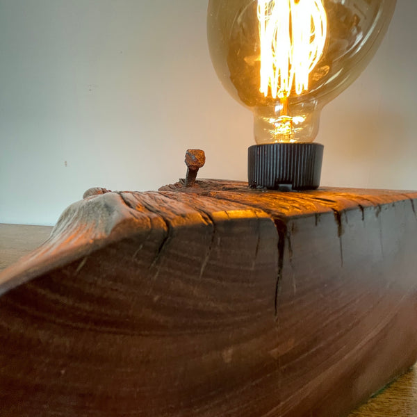 Original wharf timber table lamp handcrafted by shades at grays with edison bulb, lit, close up of smooth polished side.
