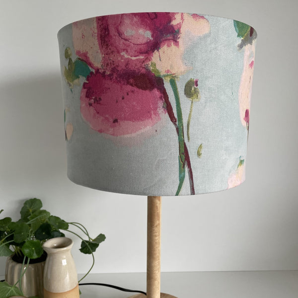 Pink blooms with green stalks on sky blue background, medium drum lampshade, unlit.