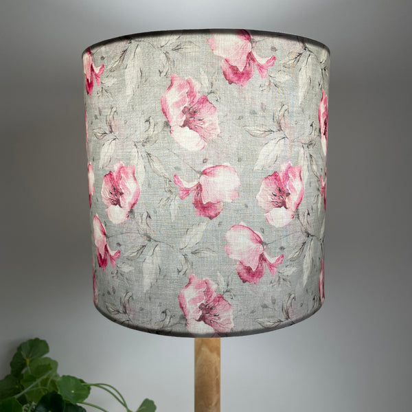 Pink rosebuds on a dove grey background, 20 cm cylinder lampshade, handcrafted by shades at grays, lit.