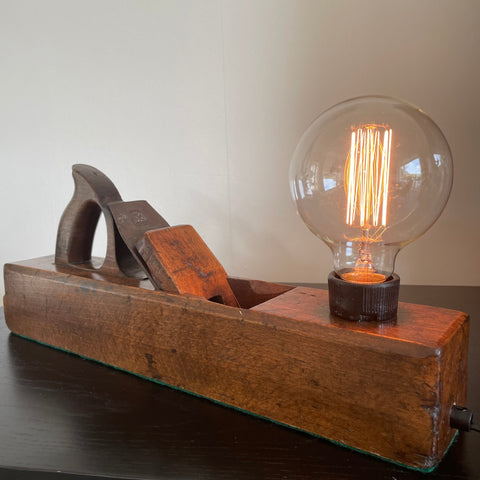 Polished beach wood of vintage lamp crafted by shades at grays from an antique carpenters' plane, with edison bulb, lit.
