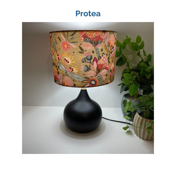 Protea fabric on medium drum lampshade and black touch base, lit, crafted by shades at grays