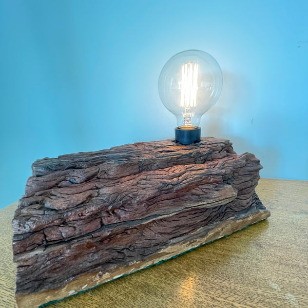 Reclaimed wood table lamp from eroded wharf timber, long front view with edison bulb, lit by Shades at Grays 