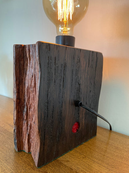 Reclaimed wood table lamp crafted by shades at grays with original bolt and replica edison bulb, lit, back and side view.