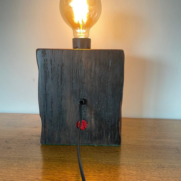 Reclaimed wood table lamp crafted by shades at grays with original bolt and replica edison bulb, lit, back view.