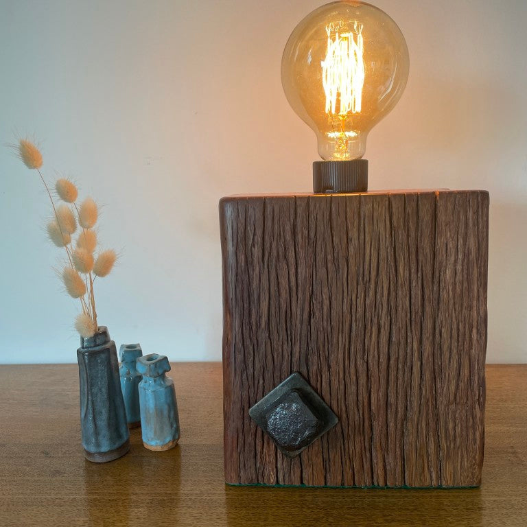 Reclaimed wood table lamp crafted by shades at grays with original bolt and replica edison bulb, lit, front view.