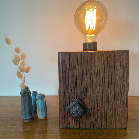 Reclaimed wood table lamp crafted by shades at grays with original bolt and replica edison bulb, lit, front view.