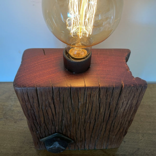Reclaimed wood table lamp crafted by shades at grays with original bolt and replica edison bulb, lit, polished top view.